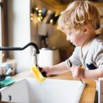 A toddler boy washing up the dishes.