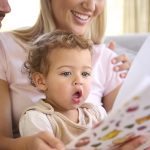 Family Sitting On Sofa At Home With Parents Reading Book With Young Son