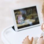 Toddler girl sitting on feeding chair watching tablet