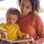 Affectionate mother reading book with adorable toddler daughter