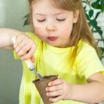 Happy little girl preparing pots with soil for planting seeds for seedlings to new spring season, little helper