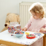 Little Girl Engrossed in Playing with Colorful Beads at Her Home Desk: Developing Motor Skills and Early Childhood Education through Play